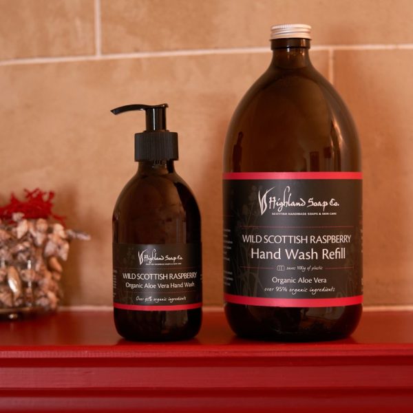 Wild Scottish Raspberry Hand Wash en Refill van The Highland Soap Company op een rode plank tegen een beige tegelmuur.