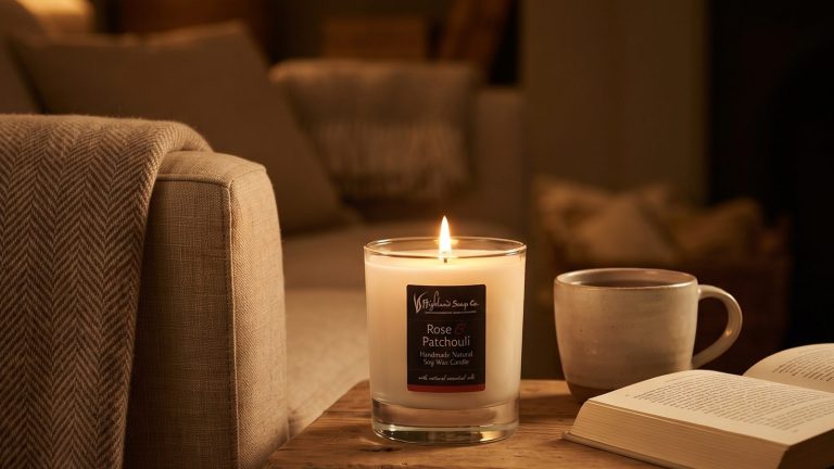 Geurkaars van The Highland Soap Company brandend op een houten tafeltje naast een kop thee en een open boek