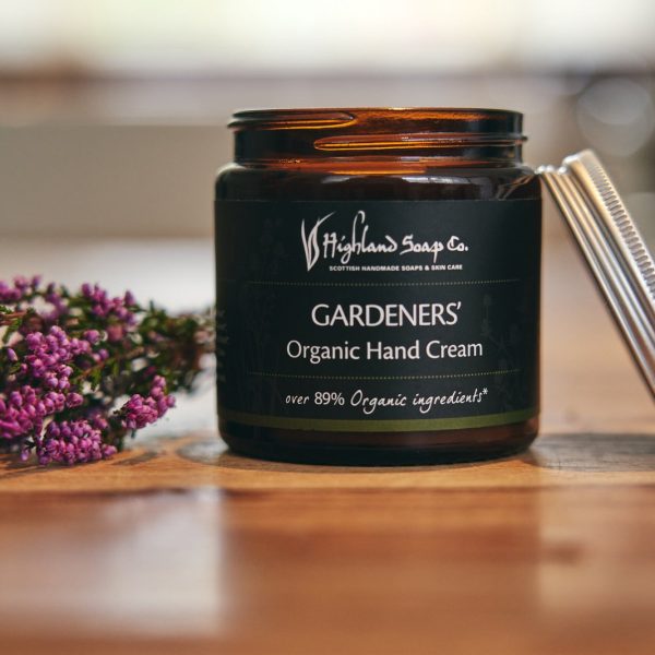 Gardeners Hand & Body Cream van The Highland Soap Company in een open pot op een houten tafel, met heide ernaast