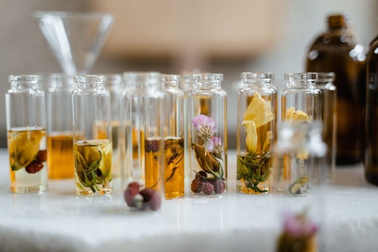 Glazen flesjes met plantenoliën en verse kruiden naast elkaar op een tafel